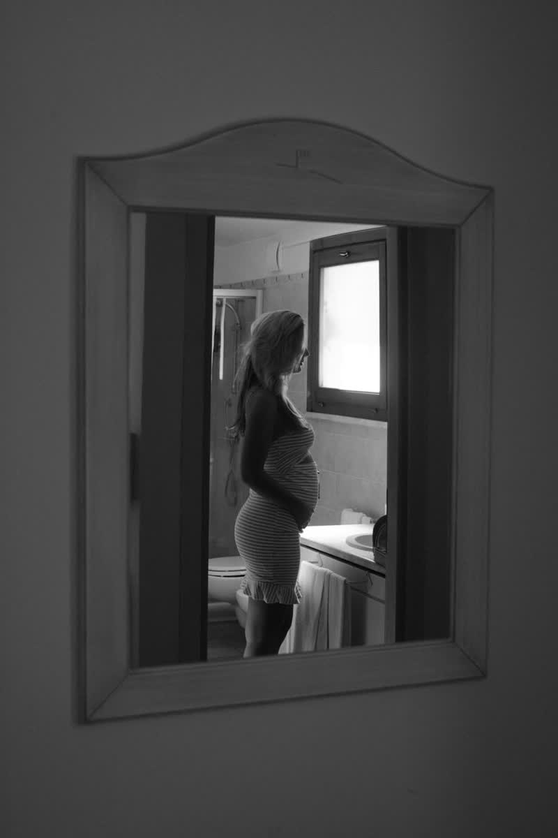 Zwart-witfoto, zwangere vrouw in profiel in de spiegel